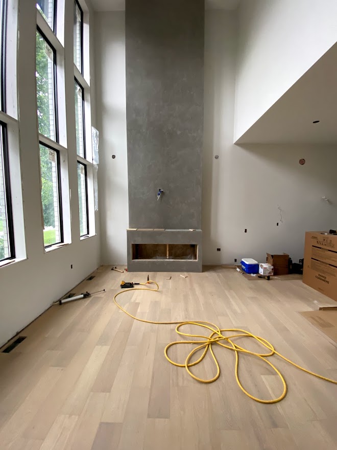 A hardwood floor in a sun room that has just been laid in front of a missing gray fireplace with an air-powered nail gun on the floor.