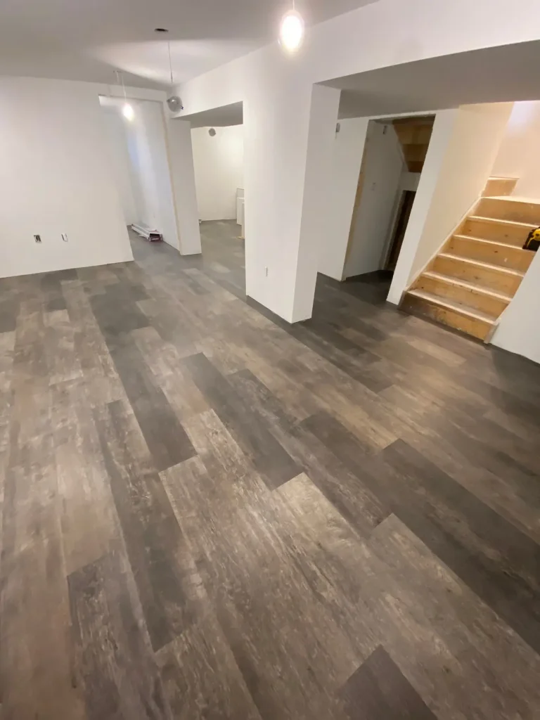 A large white room in a basement with beautiful vinyl flooring.